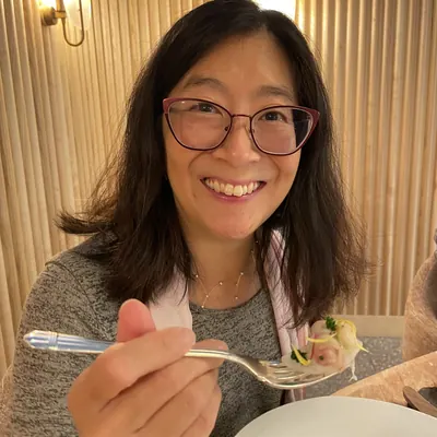 Irene smiling over a forkful of food at a restaurant table in London.