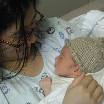 Irene cradling a sleeping newborn in a knitted hat.